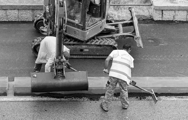 A close-up shot of road construction workers repairing a section of highway. The workers are wearing safety vests and using heavy machinery. The focus should be on the activity and effort involved in highway repairs.