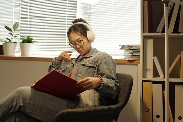 A student wearing headphones, focused on a tablet, working on a project, surrounded by books and a laptop, in a quiet study environment.