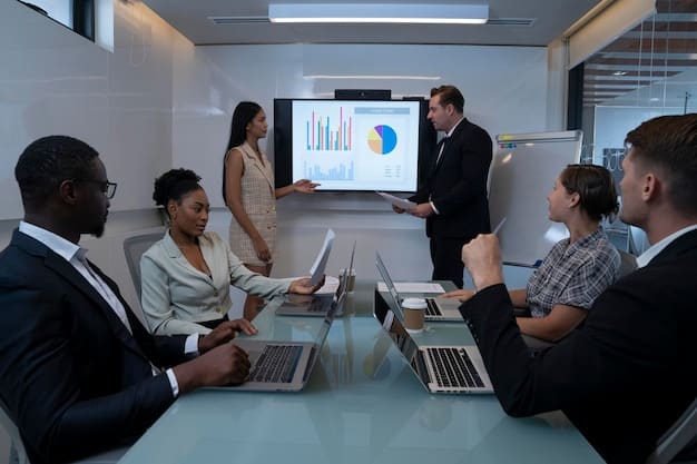 A diverse group of people sitting around a conference table, engaged in a discussion with charts and graphs displayed on a screen in the background.